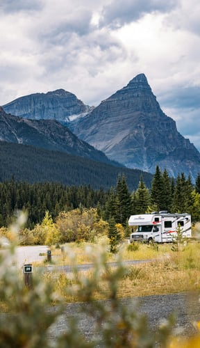 RV parked at a campsite with a dramatic rocky mountain peak rising behind autumn-coloured trees